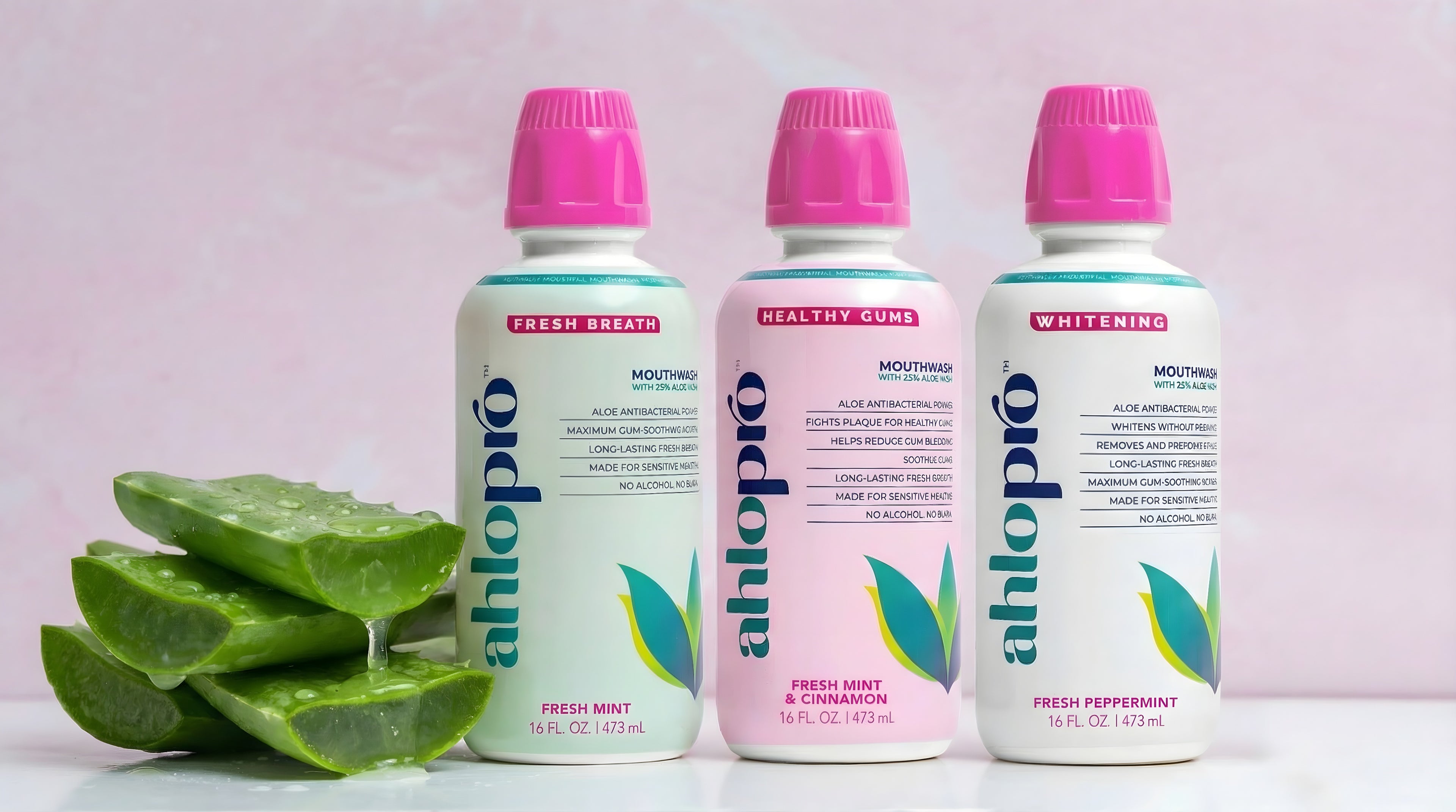 Three bottles of Ahlopio dental rinse with aloe vera leaves on a light pink background