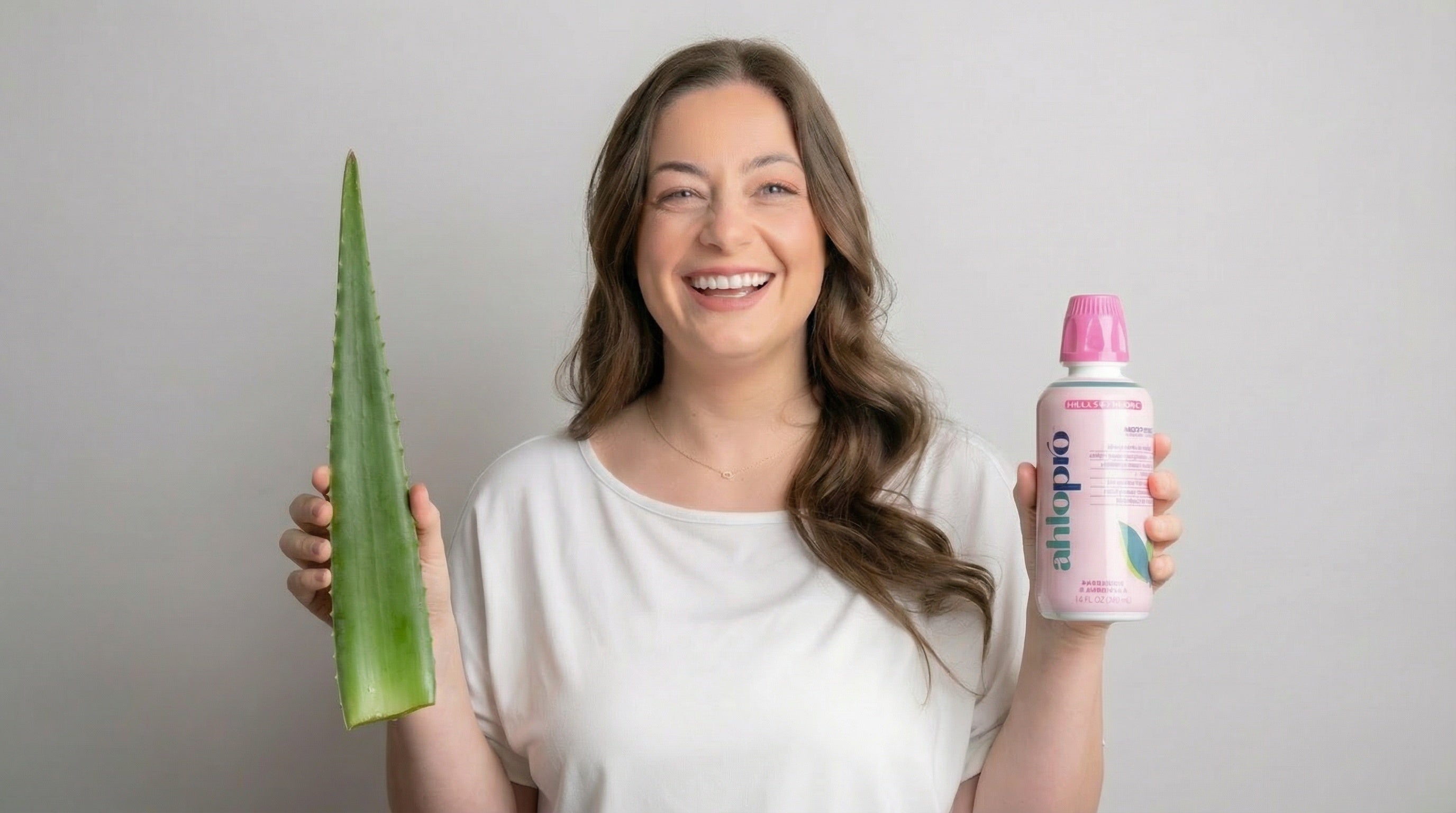 Woman holding an aloe vera plant and a bottle of Olay product against a plain background