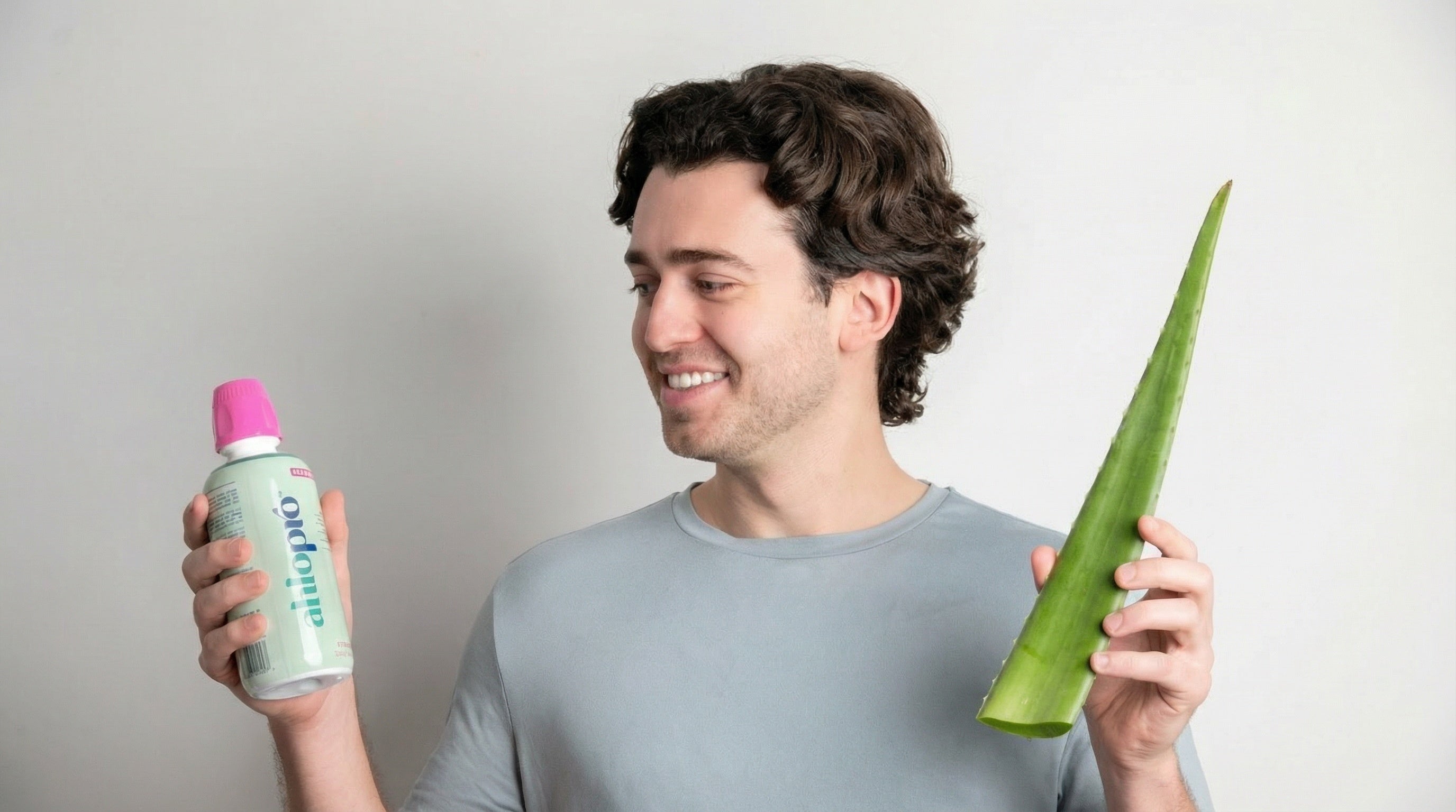 Man holding a bottle of aloe vera gel and an aloe leaf against a plain background