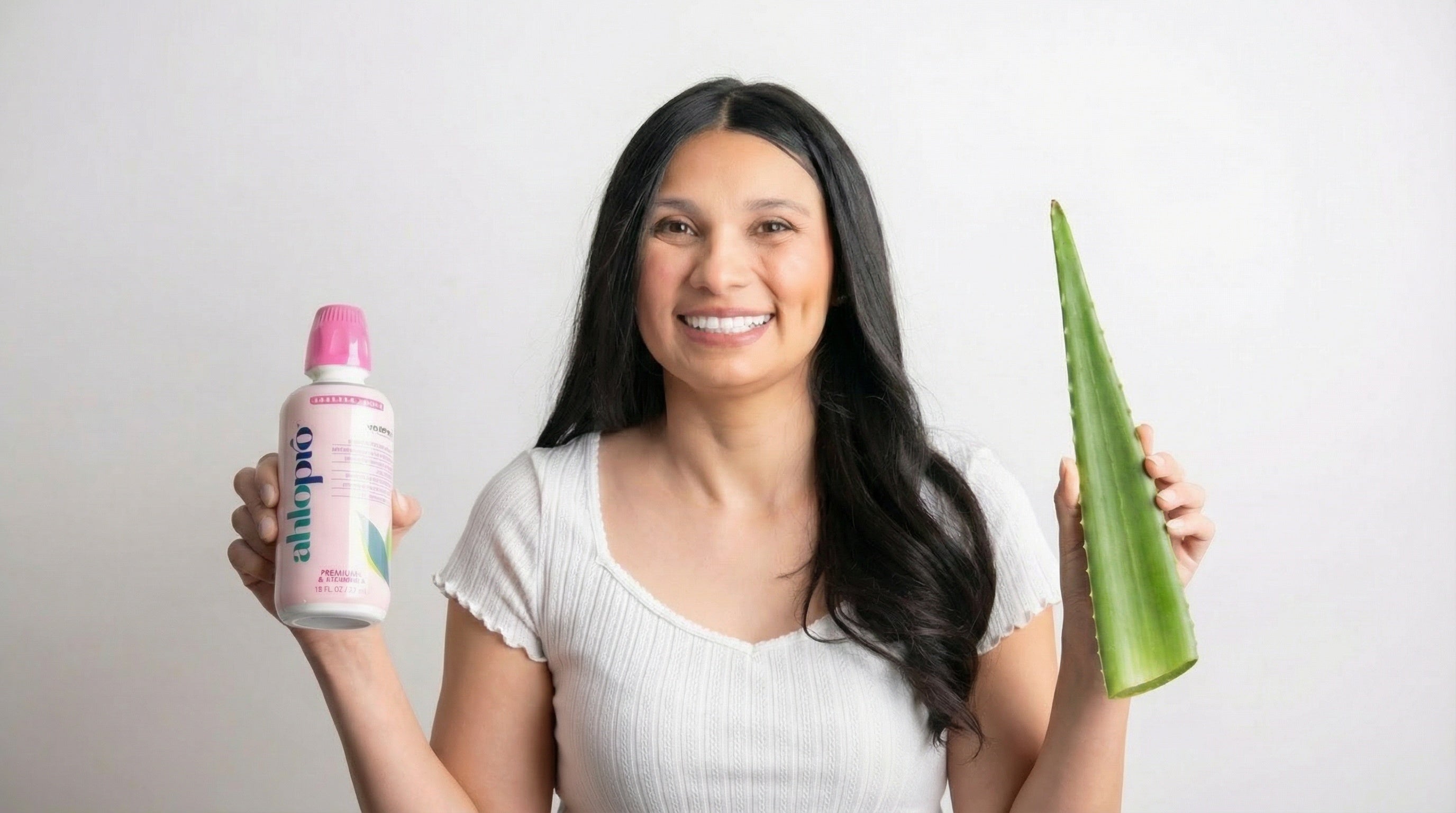 Woman holding a bottle of 'alkepro' and an aloe vera leaf against a plain background