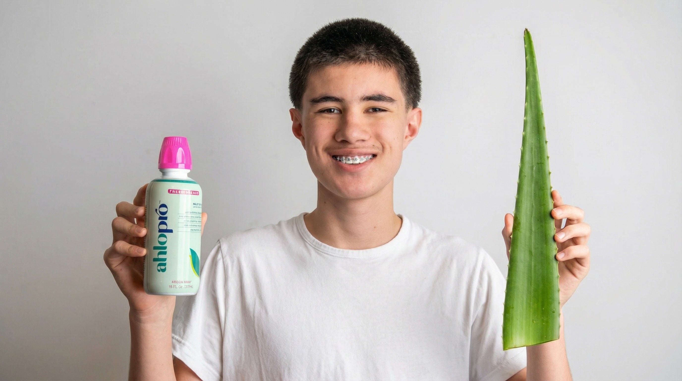 Person holding a bottle of aloe vera gel and a large aloe leaf against a plain background